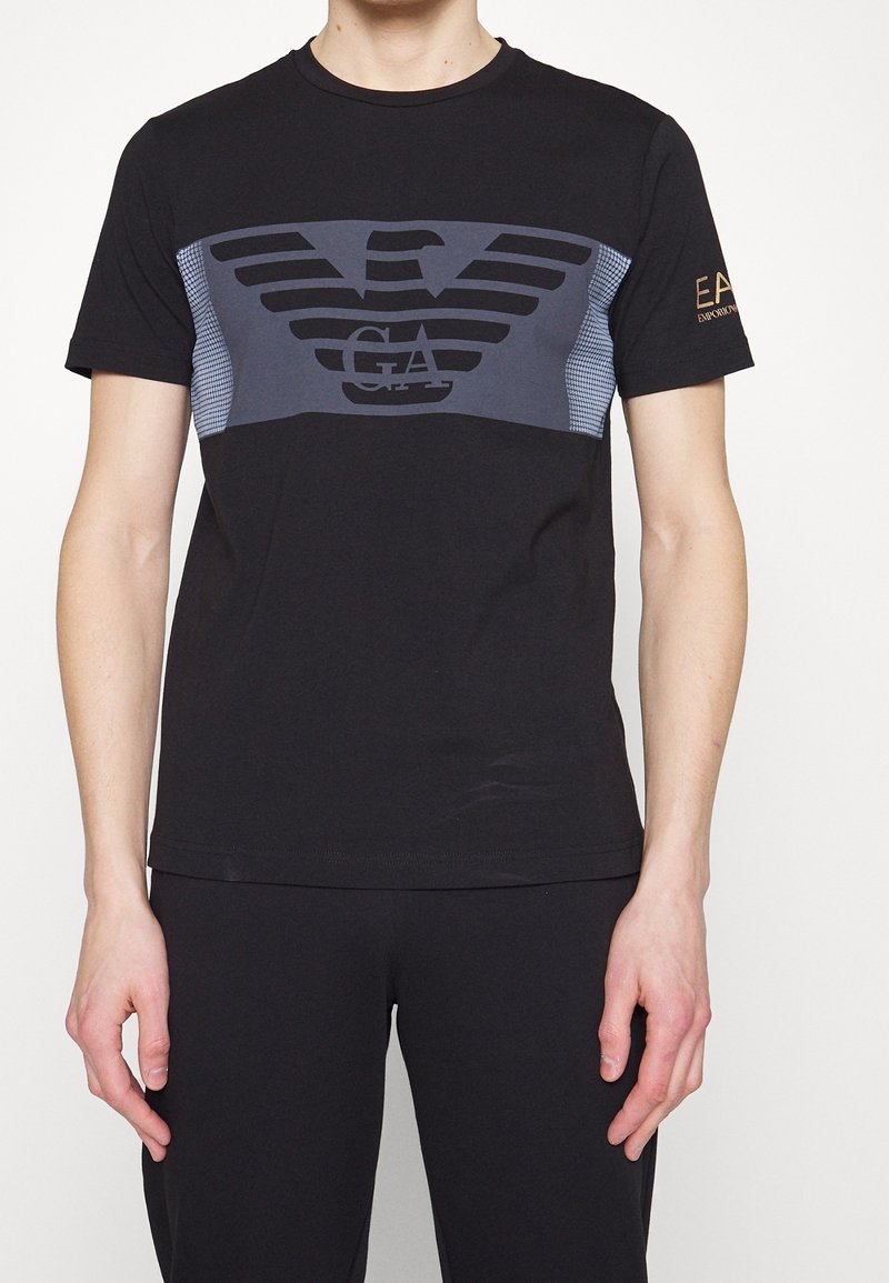 Svart bomulls-t-shirt med en grå grafisk design med vingar och logotyp, korta ärmar och rund hals. Accenterad med varumärkestext på ärmen.