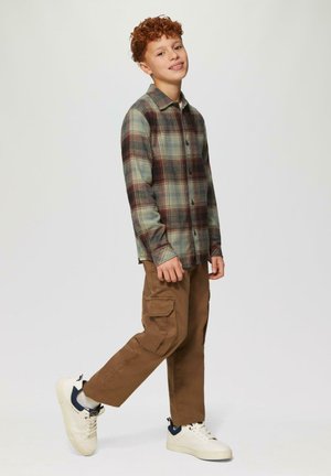 Langekleurige geruite overhemd in groen, blauw en rood, gecombineerd met bruine cargobroeken. Witte sneakers met marineblauwe accenten. Casual pasvorm en stijl.