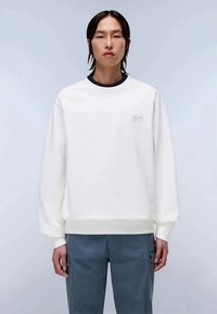 Suéter branco de mangas longas e gola redonda, com um logo subtil no peito. Combinado com calças cargo cinza. Textura suave.