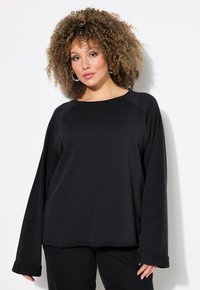 Maglia nera a maniche lunghe con scollatura rotonda e maniche raglan. Tessuto morbido con una vestibilità comoda e polsini ripiegati, abbinata a pantaloni neri.