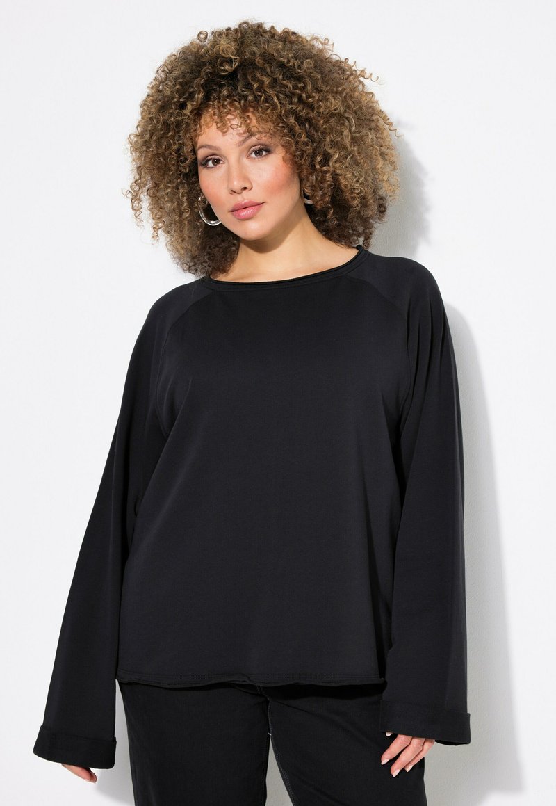 Maglia nera a maniche lunghe con scollatura rotonda e maniche raglan. Tessuto morbido con una vestibilità comoda e polsini ripiegati, abbinata a pantaloni neri.