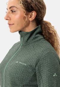 Giacca verde con zip realizzata in tessuto testurizzato, caratterizzata da un colletto alto e una cerniera a contrasto. Logo stampato sul petto e sulla manica.