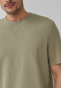 Olijfgroene T-shirt met korte mouwen, gemaakt van textuur katoen, met een ribbelhals en subtiele stiksels rond de kraag.