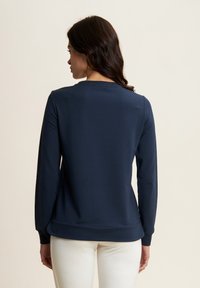 Sudadera de manga larga azul marino con cuello redondo, puños acanalados y un dobladillo ligeramente curvado, fabricada en tela suave.