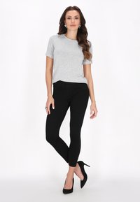 Grå kortærmet top med ribstrikkede manchetter, parret med tætsiddende sorte leggings og sorte højhælede sko. Glat tekstur, enkelt design, ingen mønstre.