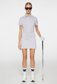 Grå polo med krage, i kombination med en matchande kort kjol. Vit golfhandske och skor. Svarta solglasögon och randiga strumpor. Golfklubba i handen.