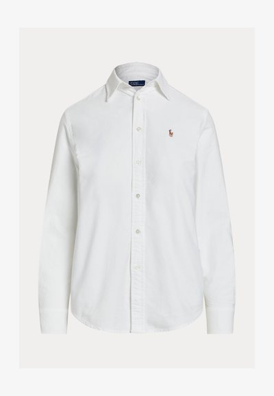 Chemise blanche à manches longues, boutonnée avec col et petit logo brodé sur la poitrine gauche, présentée sur fond uni.