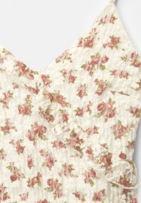 Blommig spetsblus i krämfärg med rosa rosor och gröna blad. Har volangdetaljer och en V-ringning. Lätt, strukturerad tyg.