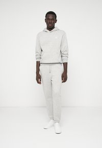 Pilkas hoodie su kengūro krepšiu ir atitinkamomis pilkomis sportinėmis kelnėmis, pagamintomis iš minkštos medžiagos, derinamas su baltais sportbačiais. Paprastas ir kasdienis stilius.