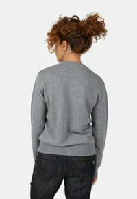 Maglione grigio lavorato a maglia con scollatura rotonda e orlo a coste, caratterizzato da una texture morbida. Abbinato a jeans scuri per contrasto.