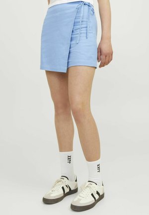 Jupe enveloppante bleu clair avec fermeture à nouer, fabriquée à partir d'un tissu doux. Portée avec des chaussettes blanches et des baskets, montrant un style décontracté.