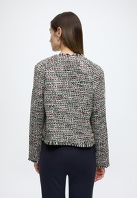 Jachetă din tweed țesut în fire multicolore, cu croială scurtă, tiv cu margine franjurată și mâneci lungi. Materialele includ un amestec de texturi și modele.