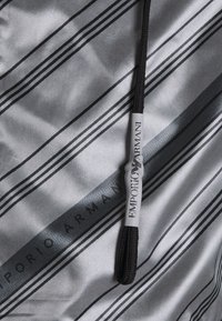 Grått tyg med svarta och grå diagonala ränder, med en märkt dragkedjetagg som har "EMPORIO ARMANI" i tydlig text.