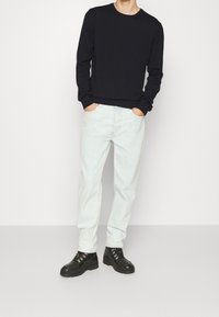 Czarna koszula z długim rękawem i okrągłym dekoltem, jasnoniebieskie dżinsy oraz czarne masywne buty. Strój charakteryzuje się luźnym krojem i prostym designem.