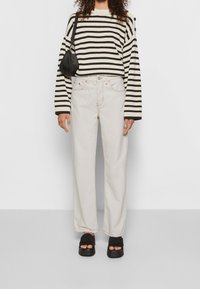 Svetr s černobílými pruhy a širokými rukávy, kombinovaný s krémovými džíny s vysokým pasem a černými platformovými sandály. Jednoduchá černá taška.