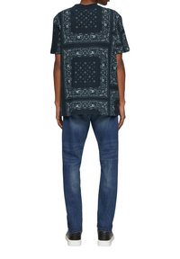 Zwarte graphic t-shirt met wit paisley patroon, korte mouwen, losse pasvorm. Gepaard met blauwe denim jeans en zwarte sneakers.