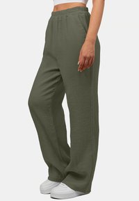 Lichte, olijfgroene, wijde broek gemaakt van gestructureerde stof met een elastische tailleband en voorzakken, gecombineerd met witte sneakers.