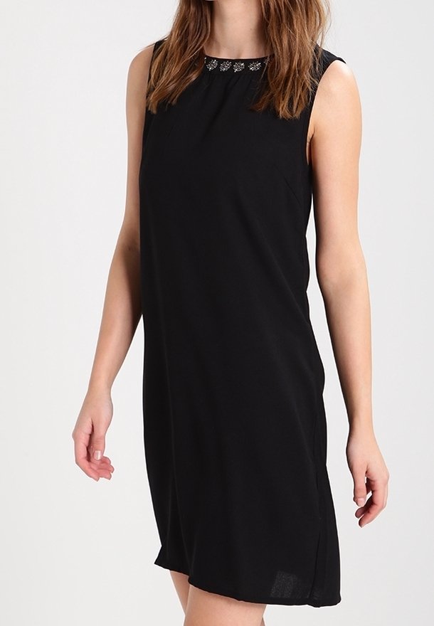 Robe noire sans manches, longueur genou, avec un col rond orné de petites décorations florales argentées, portée par une personne debout.