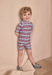 Badeset für Kinder bestehend aus einem kurzärmeligen Oberteil und Shorts. Hergestellt aus leichtem Stoff mit einem Muster aus Soldaten in Rot und Blau auf weißem Hintergrund.