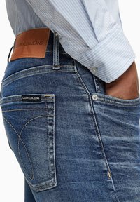 Džínové kalhoty ve střední modré barvě s jemným vyšisováním. Obsahují koženou nášivku s logem a dekorativní švy. Úzký střih.