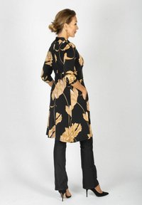 Sukienka w kwiatowy wzór w czerni z beżowymi kwiatami, z rękawami 3/4 i kieszeniami po bokach. Połączona z czarnymi spodniami i wysokimi obcasami.