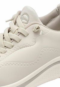 Light beige sneaker with textured leather upper, padded collar, and flat laces. Features a rounded toe and subtle logo detail on the tongue.