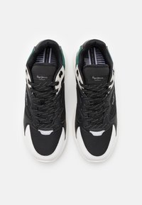 Baskets noires et grises avec une tige en mesh, des accents blancs et un talon vert. Elles possèdent des lacets ronds et un col texturé et rembourré.