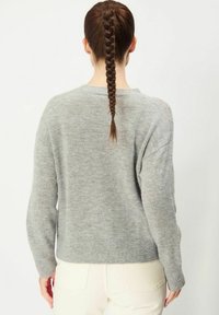 Grå stickad tröja med avslappnad passform, ribbade ärmslut och nederkant. Mjuk textur med ett subtilt mönster. Bakvyn visar en enkel, ren design.