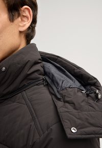 Giubbotto imbottito nero con colletto alto, caratterizzato da una texture trapuntata, una cerniera interna e una fodera nera a contrasto.