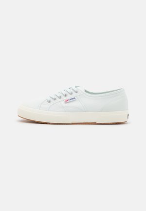 Biały niskoprofilowy tenis z płótna z beżową gumową podeszwą, białymi sznurówkami oraz metką z logo Superga po boku.