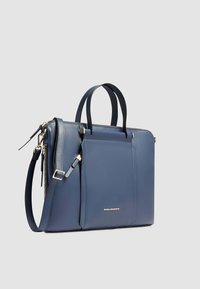 Sac à main en cuir bleu avec doubles poignées, bandoulière réglable, fermeture éclair, poche avant et logo discret sur le côté.