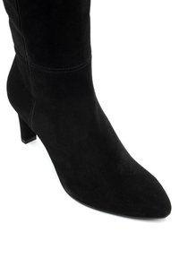 Botín de ante negro con puntera afilada, tacón moderado y textura suave. Presenta detalles cosidos en la parte superior.