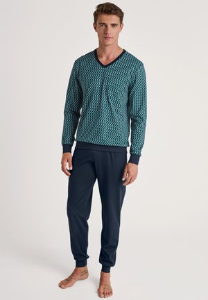 Langärmliges V-Ausschnitt-Oberteil in Teal mit Diamantmuster, kombiniert mit dunkelblauen, schmal zulaufenden Sweatpants. Weicher Stoff mit gerippten Bündchen.