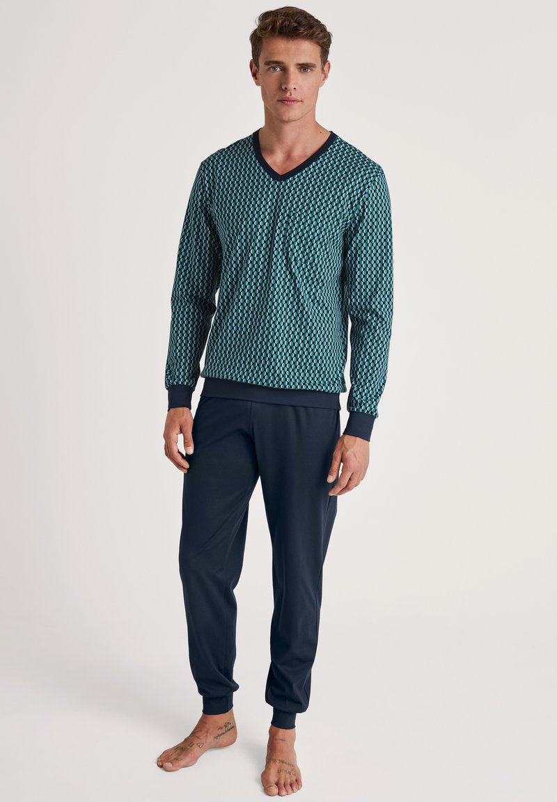 Langarm V-hals top in teal met een ruitpatroon, gecombineerd met donkerblauwe geplooide joggingbroek. Zacht materiaal met geribbelde manchetten.