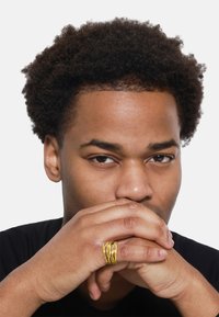 Une bague en or torsadée portée sur une main, présentant de multiples brins entrelacés avec une texture lisse sur un fond sombre.