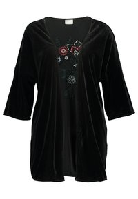 Veste en velours noir à l'avant ouvert avec des manches trois-quarts sur un haut présentant un motif floral brodé en rouge, blanc et vert.