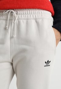 Ljusbeige sweatpants i mjukt tyg med resår i midjan och dragsko samt en svart Adidas-logga på vänster höft.