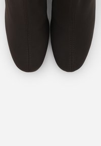 Svart fotbeklädnad med en slät, matt yta. Har en rundad övre design och kontrasterande sömnadsdetaljer. Rundad tåform.