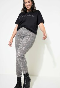 T-shirt nera con testo bianco in corsivo abbinata a pantaloni grigi con stampa animale e stivali platform neri. Outfit casual con motivi testurizzati.