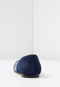 Granatowe zamszowe płaskie buty z okrągłym noskiem i gładkim przodem. Posiadają niski obcas i minimalne przeszycia dla czystego designu.