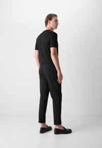 Tricou negru cu mânecă scurtă, asociat cu pantaloni negri din stofa. Pantalonii au tiv rulat. Modelul poartă încălțăminte neagră tip slip-on.