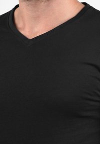Melnas V-veida kakla t-krekls no mīkstas kokvilnas, ar gludu tekstūru un pieguļošu dizainu. Minimālas šuves izceļ kakla izgriezumu un audumu.