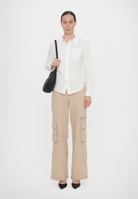 White long-sleeve button-up shirt with a chest pocket, paired with beige cargo pants featuring large pockets and a zippered pocket. Black handbag and heels.