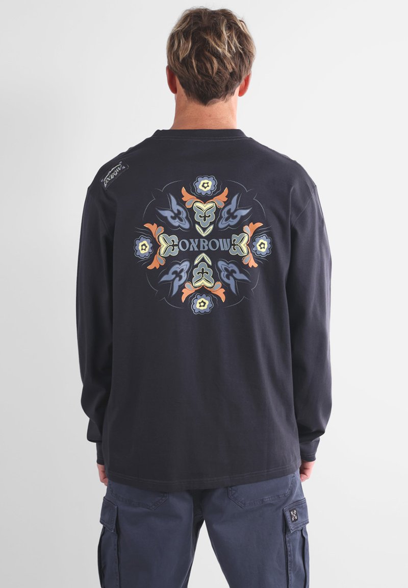 T-shirt à manches longues bleu marine foncé avec un graphisme central aux couleurs pastel, comprenant des motifs floraux et ornementaux. Coupe standard avec des bords côtelés.