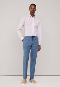 Chemise à rayures à manches longues en blanc et rose, associée à un pantalon bleu avec cordon de serrage et des chaussures beige à enfiler. Tissu lisse, coupe ajustée.