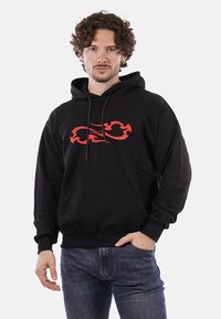 Felpa nera con cappuccio in cotone, caratterizzata da una grafica di fiamme rosse sul davanti, cappuccio con cordino e tasca a marsupio frontale.