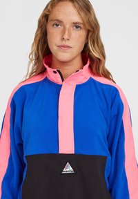 Fleece pullover i blå, pink og sort. Høj krave med halvdels lynlås; logo på forsiden. Blød tekstur med farveblokdesign.