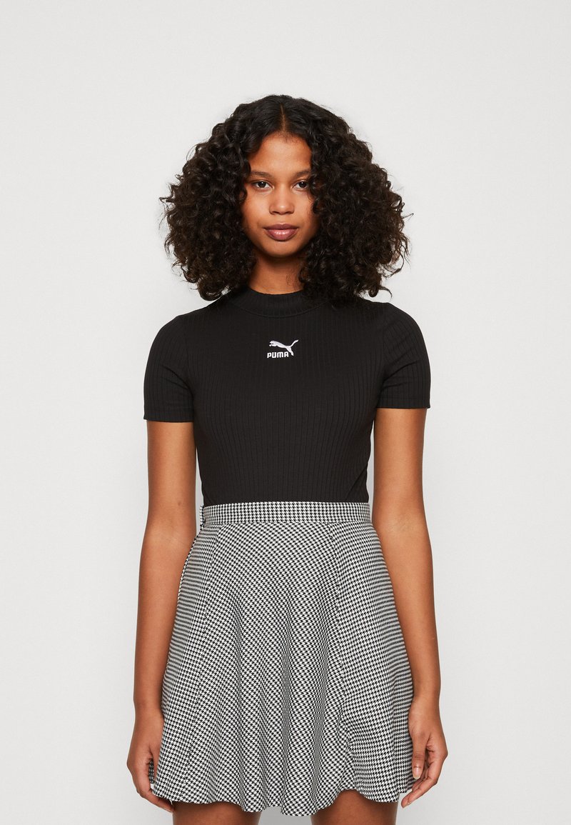 Sort ribbet kortærmet top med Puma-logo, parret med en sort og hvid houndstooth nederdel, med flagrende design og tekstureret stof.