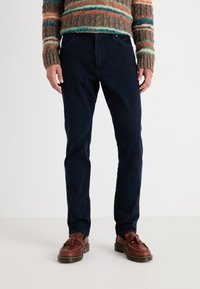 Vaqueros azul marino en un diseño ajustado, con un estilo clásico de cinco bolsillos y costuras sutiles. Combinados con zapatos de cuero marrón.