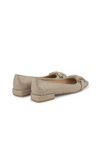 Beżowe płaskie buty z zaokrąglonym noskiem, ozdobione metalowymi ćwiekami, akcentem w postaci kokardki oraz niskim obcasem w formie klocka. Gładka tekstura, minimalistyczny design.